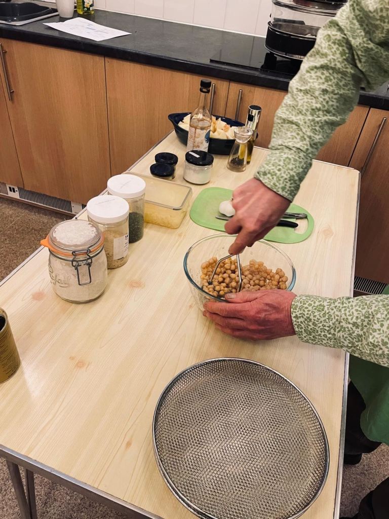 Photo of a person using a potato masher to mash chickpeas for this recipe.  Also shows ingredients containers and trays for the air-fryer